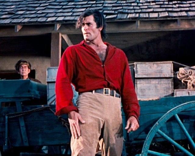 Clint Walker in his iconic red shirt, ready for action, as seen in one of his memorable film roles, displaying his commanding presence