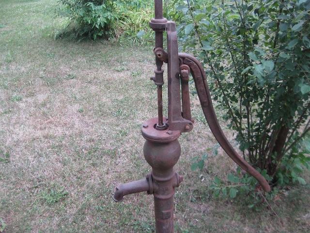 A vintage Fairbury hand pitcher pump standing tall in the garden, a relic from the days when water was drawn by hand.