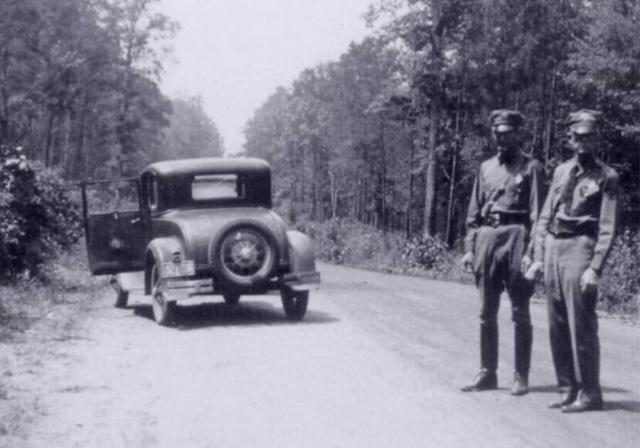 Two police officers survey the site of Bonnie and Clyde's ambush along Louisiana State Highway 154 near Sailes
