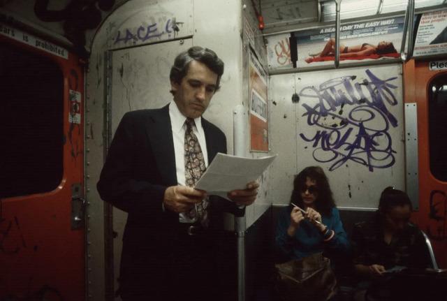 A lone commuter is absorbed in a book, a brief moment of quiet amidst the fast-paced rhythm of subway life in 1981.
