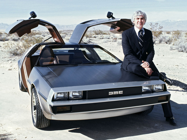 John Z. DeLorean stands beside the DeLorean DMC-12, showcasing its iconic gull-wing doors. The brushed stainless steel body and distinct design made the car a symbol of innovation in the automotive industry.