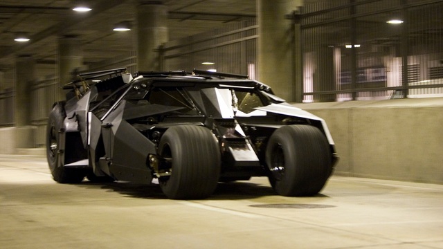 The Batmobile Tumbler in motion through an underground parking garage, showcasing its aggressive design and raw power.
