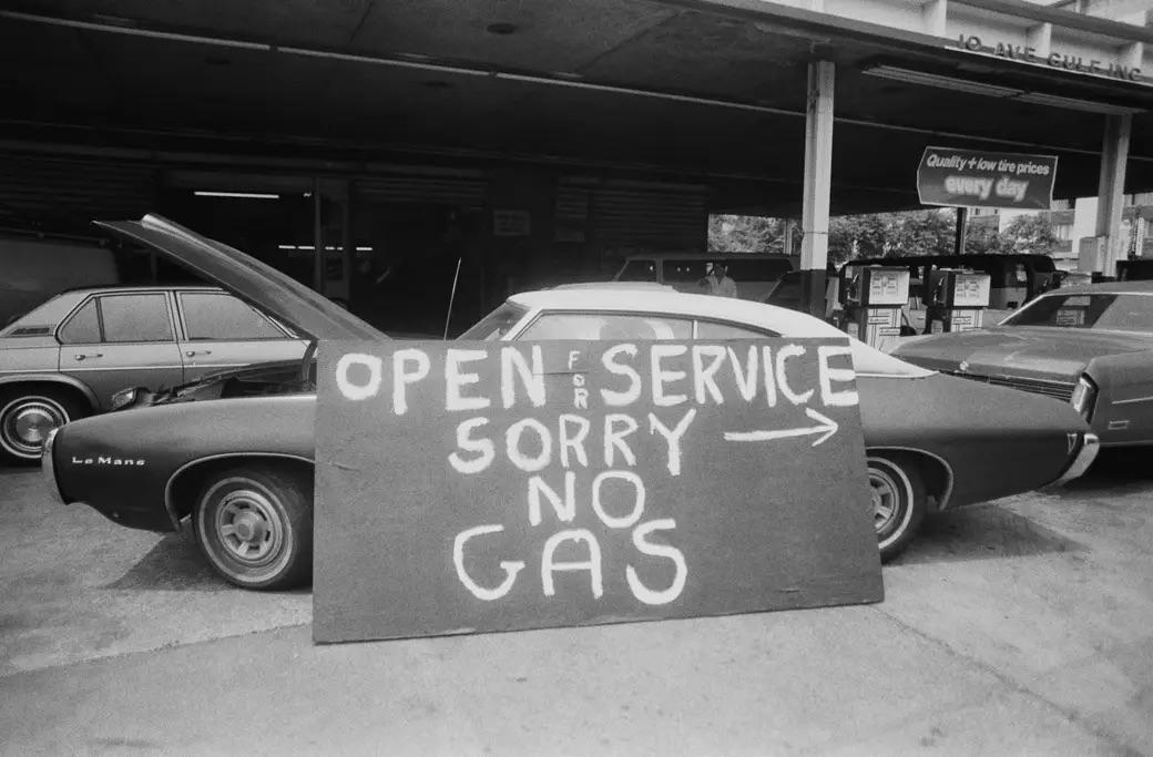 In the midst of New York's 1970s gasoline shortage, a weathered sign leans against a car—a silent witness to an era defined by scarcity and resilience.