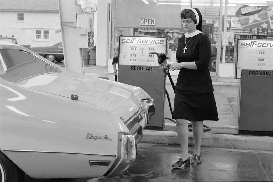 At a self-service station in 1975, a nun skillfully fills her Buick Skylark—a unique blend of faith and everyday