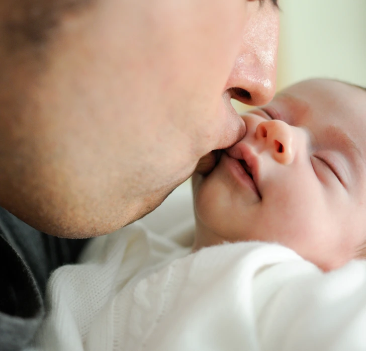 An innocent moment of a parent kissing their newborn, a reminder of how easily infections like herpes simplex can spread through such gestures.