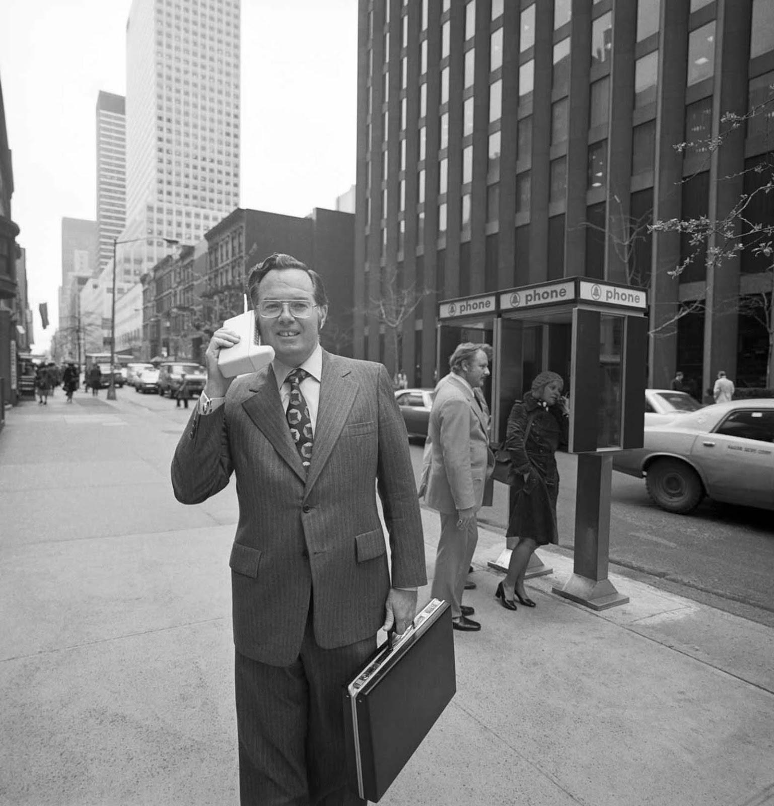 In 1973, John Mitchell, standing on the bustling streets of New York, proudly holds the device he helped design—the world’s first mobile phone