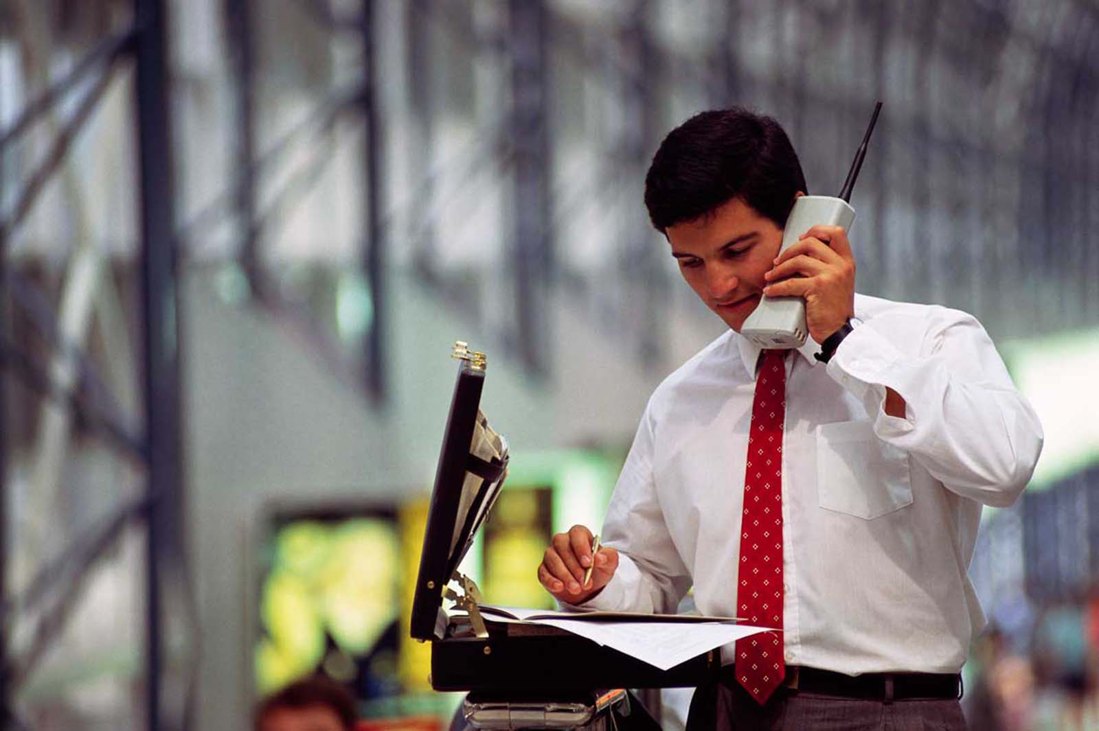 In 1990, a young businessman meticulously goes over figures on a massive cell phone, symbolizing the start of a new age in communication.