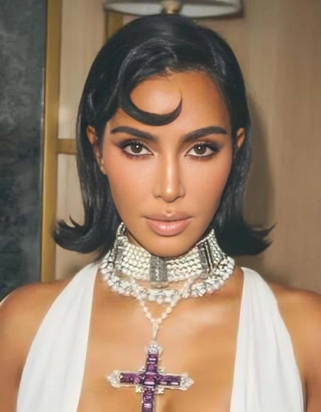 Kim Kardashian in a striking black outfit, sporting a bold hairstyle and unique cross necklace, at a high-profile event.