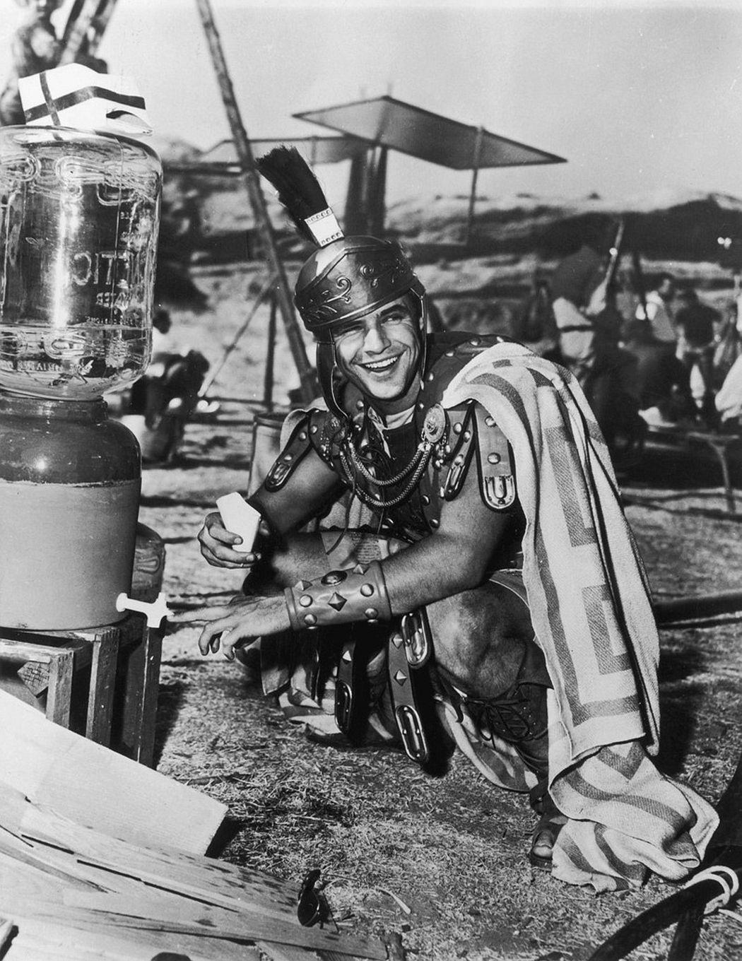 Marlon Brando enjoys a light moment on set, dressed in costume as a Roman gladiator.
