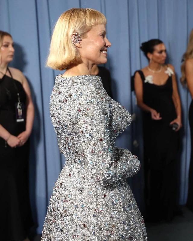 Pamela Anderson from a side angle, embracing her sparkling outfit and chic new hairstyle.