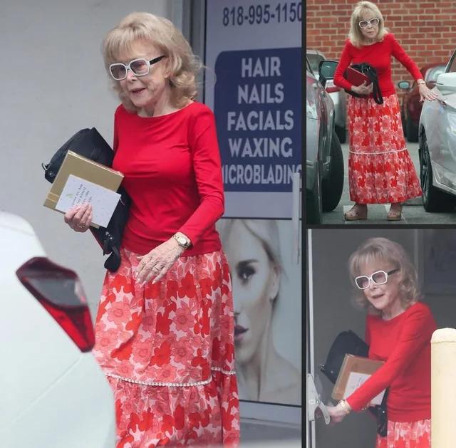 Wearing a red long-sleeve blouse paired with a patterned skirt, tan sandals, and white sunglasses, she looked effortlessly chic.