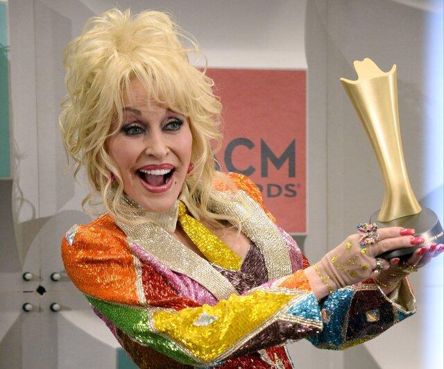 Dolly Parton with her signature joyful smile, proudly holding an award at the ACM Awards, celebrating her unmatched contributions to country music.
