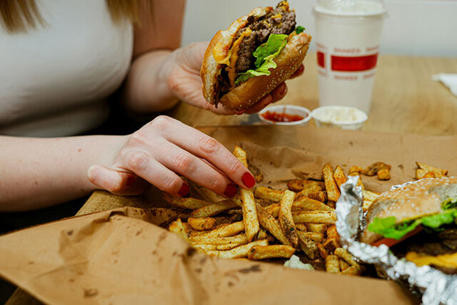 A person reaching for fast food and fries, emphasizing the role of highly processed diets in modern dietary habits.