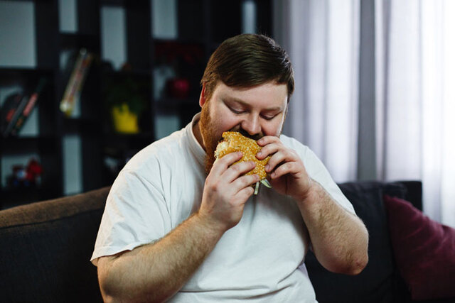 An individual eating a fast-food burger, representing the caloric density common in contemporary convenience lifestyles.